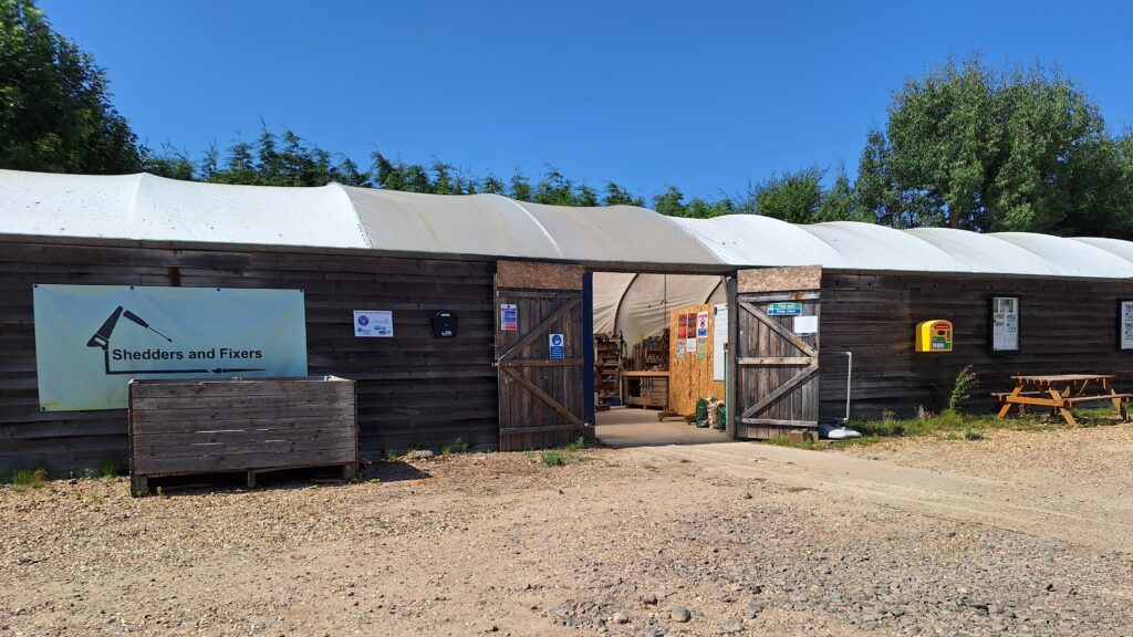 Photo of Shedders and Fixers premises with it's polytunnel roof and car parking area outside